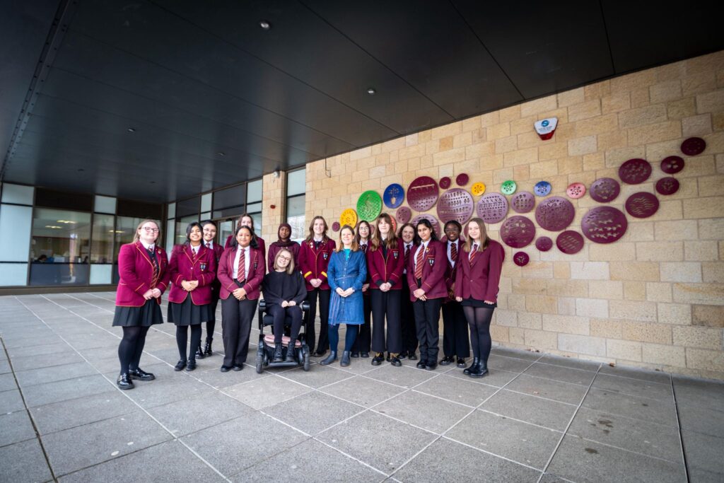 Pupils from Harris Academy standing outside the school with Louise Kirby all smiling next to the circular artworks on the front of the building